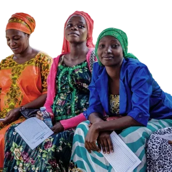 A photo of a group of African women in traditional dress, sat in a row on a bench holding paperwork while they wait for appointments.