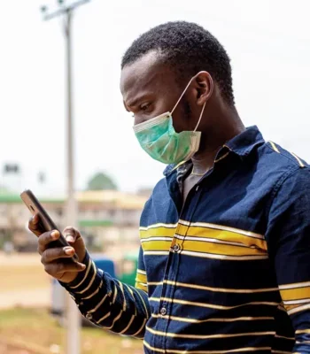 Photo of an African man standing outdoors, looking at a mobile phone.