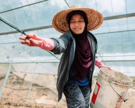 A photo of an Asian female farmer throwing soil onto the ground.