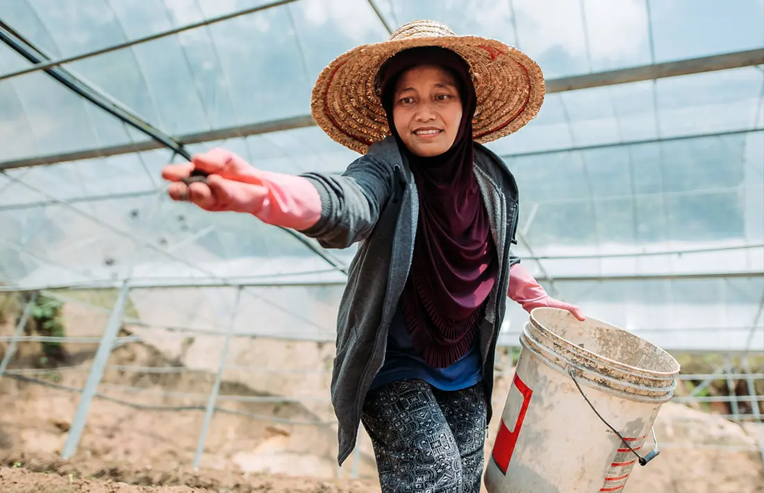 A photo of an Asian female farmer throwing soil onto the ground.