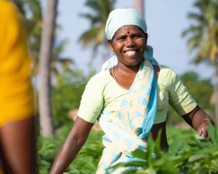 A photo of a smiling South Asian farm worker in a field.