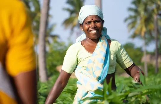 A photo of a smiling South Asian farm worker in a field.