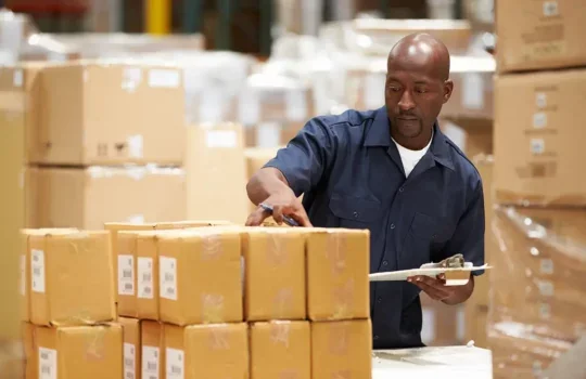 Photo of a middle aged black man in a warehouse, checking boxes