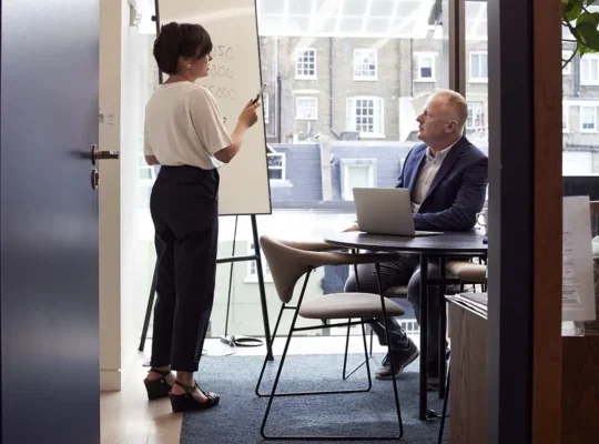 Male and female senior co-workers next to a whiteboard in an office