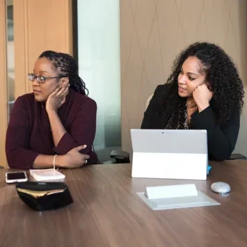 Two women in a meeting room listening to someone speak