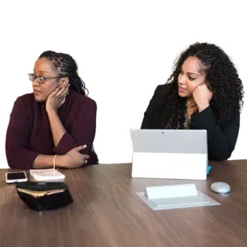 Two women in a meeting room listening to someone speak