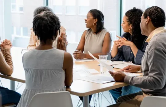 A photo of a diverse group of people having a discussion around a meeting table.