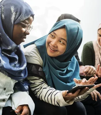 A photo of a small group of young women wearing headscarfs, talking and looking at a mobile phone.