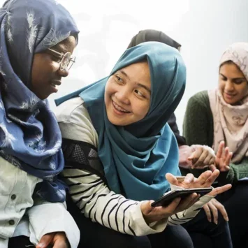 A photo of a small group of young women wearing headscarfs, talking and looking at a mobile phone.