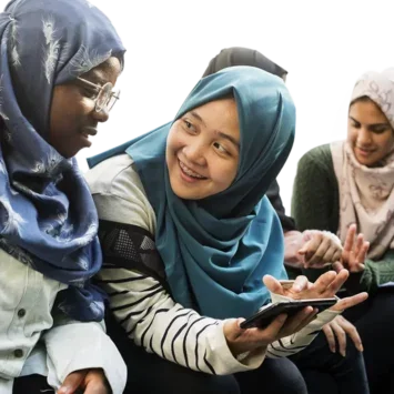 A photo of a small group of young women wearing headscarfs, talking and looking at a mobile phone.