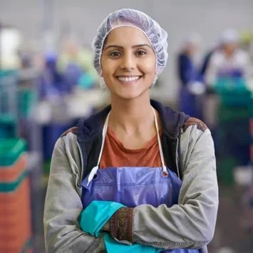 Female factory worker wearing a hairnet and apron, smiling at the camera