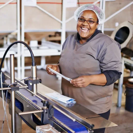 Photo of female factory worker smiling and laughing whilst stood at a machine.