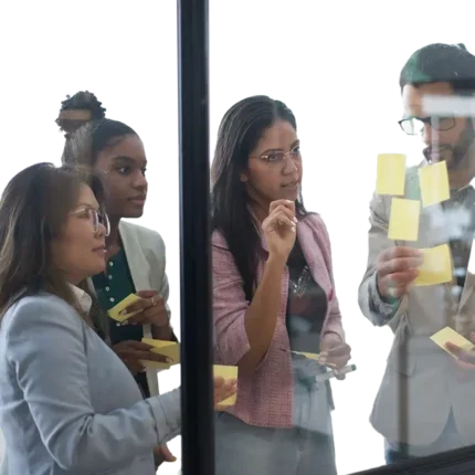 Group of colleagues collaborating in an office, looking pensively at some sticky notes on a glass wall.